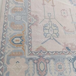 May include: A beige rug with a light blue and pink floral pattern. The rug has a border with a geometric design.