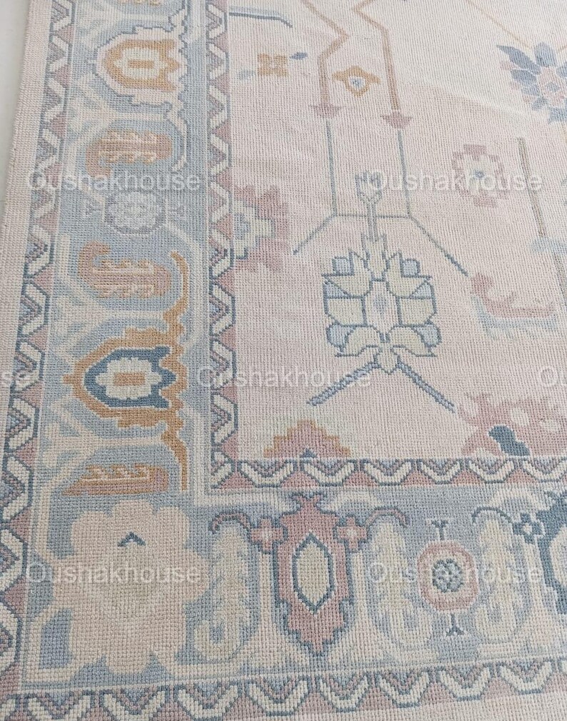 May include: A beige rug with a light blue and pink floral pattern. The rug has a border with a geometric design.