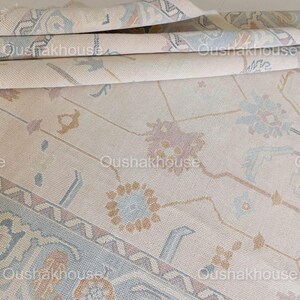 May include: A beige rug with a geometric pattern in shades of blue, brown, and pink. The rug has a subtle sheen and a soft texture.