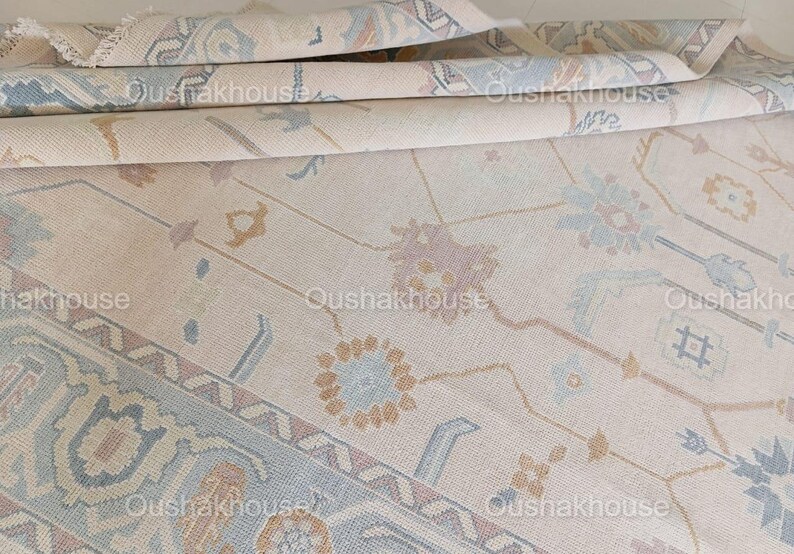 May include: A beige rug with a geometric pattern in shades of blue, brown, and pink. The rug has a subtle sheen and a soft texture.