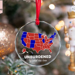 May include: A clear glass bauble featuring a red and blue map of the United States. The bauble has the text "UNBURDENED by what has been" printed on it.