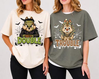 May include: A cream t-shirt featuring a cartoon chipmunk dressed as Frankenstein with the text DOUBLE, and a dark olive green t-shirt featuring a cartoon chipmunk dressed as a mummy with the text TROUBLE, both with spiderweb and bat graphics.