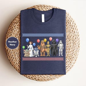 A navy blue t-shirt with a graphic design featuring various characters from popular media, including a baby star, a robot, a character with a balloon, and a character in a stormtrooper outfit.