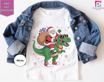 Maglietta di Babbo Natale a cavallo di un dinosauro, maglietta di Natale divertente Trex, maglietta regalo per bambini, maglietta di Natale 2025, maglietta di Babbo Natale Trex, maglietta di Natale per bambini