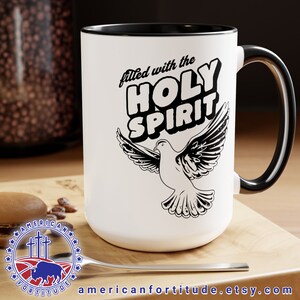 Puede incluir: Taza de cerámica blanca con borde y asa negros. La taza tiene un gráfico en blanco y negro de una paloma con el texto "filled with the HOLY SPIRIT" en una fuente retro.
