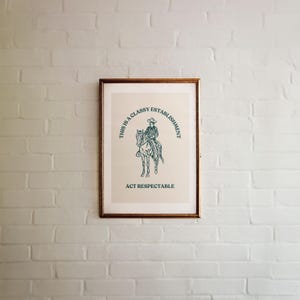 Może przedstawiać: Wydruk w ramie z beżowym tłem i zieloną ilustracją kowboja na koniu. Tekst wok&oacute;ł ilustracji brzmi "This is a Classy Establishment Act Respectable".