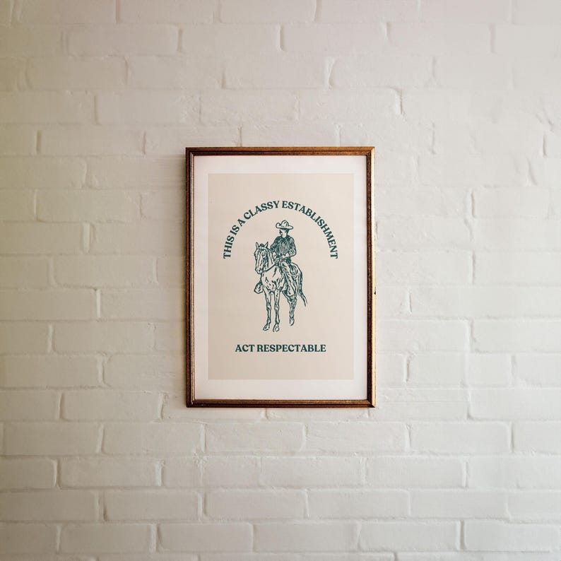 Może przedstawiać: Wydruk w ramie z beżowym tłem i zieloną ilustracją kowboja na koniu. Tekst wok&oacute;ł ilustracji brzmi "This is a Classy Establishment Act Respectable".