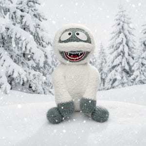 May include: A handmade, plush abominable snowman toy. The snowman is white with gray accents on the head, hands, and feet. It has a wide, toothy grin with a red mouth and is sitting in the snow with a snowy forest background.