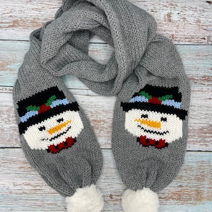 Könnte beinhalten: Grauer Strick Schal mit einem Schneemann-Design an jedem Ende. Der Schal hat weiße Bommeln an den Enden.
