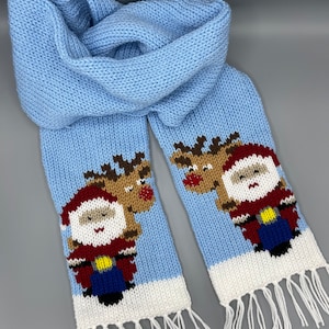 May include: A light blue knitted scarf with white fringe. The scarf features a knitted design of Santa Claus and a reindeer riding a motorcycle.