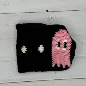 Pode incluir: Um fantasma de crochê preto e rosa com olhos brancos. O fantasma é um design plano de crochê.