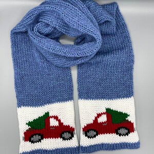 May include: A blue knitted scarf with white stripes and red truck designs carrying Christmas trees.
