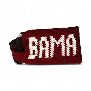 May include: A knitted headband in crimson red with the word "BAMA" in white block letters. The headband is folded over, revealing a section of brown and white knit. The accessory is designed for headwear.