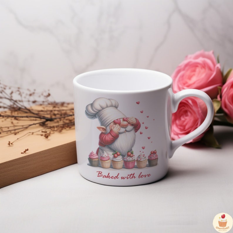 May include: White ceramic mug with a cartoon gnome wearing a chef hat and covering its eyes with hearts. The gnome is surrounded by cupcakes with pink and white frosting and red cherries. The text "Baked with love" is printed below the cupcakes.