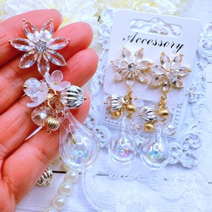 May include: A pair of dangle earrings with a clear crystal snowflake charm and a teardrop shaped glass bead. The earrings are on a white card with the word "Accessory" printed on it.
