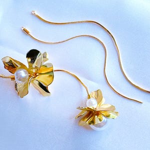 May include: A pair of gold flower earrings with a pearl accent. The earrings are on a white background.