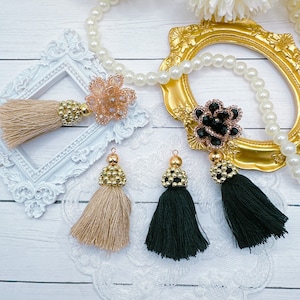 May include: Two sets of tassel embellishments with gold beads and a flower charm. One set is beige and the other is black.