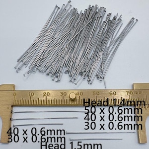 May include: A collection of silver-colored metal head pins for jewelry making. A brass caliper shows measurements of 30mm, 40mm, and 50mm lengths with 0.6mm thickness. The text indicates head sizes of 1.4mm and 1.5mm for these straight metal pins.