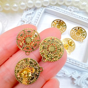May include: Close-up of several gold-colored filigree earring components. The components are round with a floral design and a small loop for attaching to other jewelry pieces. The earrings are on a white background.