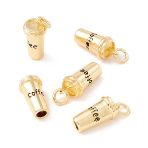 May include: Gold-colored coffee cup charms with the word "coffee" printed on the side. The charms have a small loop at the top for attaching to jewelry or other crafts. The charms are in a variety of positions.