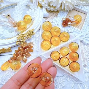 May include: A collection of amber glass beads in various sizes, displayed on a white surface. The beads are round and have a smooth, polished finish. Some of the beads are arranged in a triangular shape, while others are scattered around the surface.