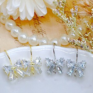 May include: A pair of silver and gold earrings with a bow design made of clear rhinestones.