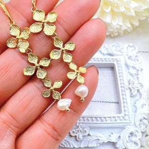 May include: Gold flower-shaped earrings with a dangling pearl accent. The earrings are made of a delicate metal and have a floral design.