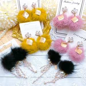May include: Three pairs of faux fur earrings with crystal embellishments. The earrings are displayed on white card stock with the words "Fashion Jewelry" and "Accessory" printed on them. The earrings are in black, pink, and yellow.