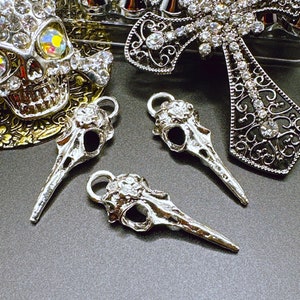 May include: Three silver bird skull charms with intricate details. Each charm has a loop at the top for attaching to jewelry or other crafts.