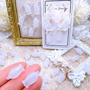May include: White flower-shaped resin earrings with gold accents. The earrings are displayed on a white background with a white lace overlay. The earrings are also shown in a close-up view, with a hand holding two of the flower-shaped resin pieces.