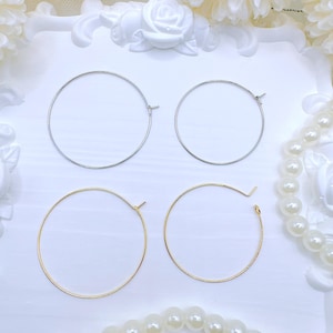May include: Four hoop earrings, two silver and two gold, displayed on a white surface. The earrings are all circular in shape and have a simple design.