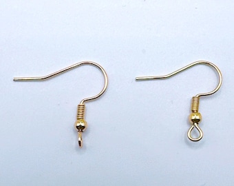 Puede incluir: Dos ganchos dorados para pendientes. Cada gancho tiene un alambre curvado para la oreja, un resorte en espiral, una pequeña cuenta y un lazo o un pequeño gancho en la parte inferior para sujetar un dije o una cuenta. Los ganchos están sobre un fondo blanco.