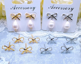 Puede incluir: Dos pares de pendientes de perlas con detalles de lazo en oro y plata. Los pendientes se muestran en tarjetas blancas con la palabra "Accesorio" impresa en ellas. También hay varios hallazgos de pendientes de lazo sueltos en oro y plata.