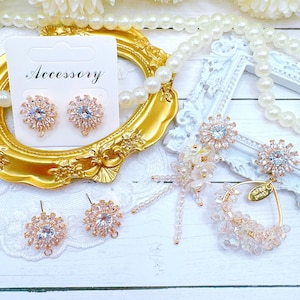 May include: A collection of jewelry pieces, including earrings and a pendant, arranged on a white surface. The earrings and pendant feature a floral design with clear and light blue crystals. The word "Accessory" is printed on a white card.