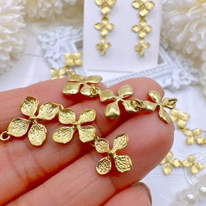 May include: Gold-toned metal flower charms with a textured surface. The charms are connected by small loops and are arranged in a cascading pattern.