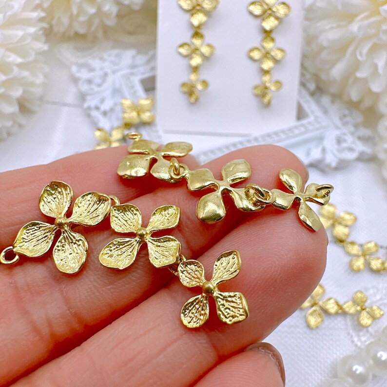 May include: Gold-toned metal flower charms with a textured surface. The charms are connected by small loops and are arranged in a cascading pattern.