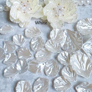May include: White floral embellishments and pearl beads are displayed. The image features two large, layered flower designs with gold-colored centers. Scattered around are numerous white, petal-shaped pieces. The word "White" is printed on the image.