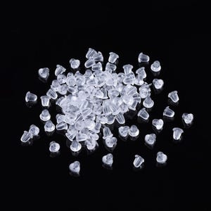 May include: A large quantity of clear plastic earring backs. The backs are small and have a rounded top.