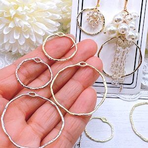 May include: A collection of gold and silver-toned hoop earring components. Some hoops have a hammered texture. Two pairs of earrings are displayed, one with clear crystals and the other with white pearls.