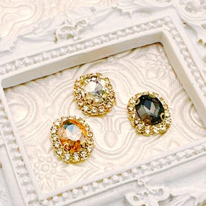 May include: Three oval-shaped rhinestones with gold settings. The rhinestones are clear, peach, and black.