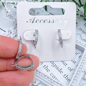 May include: A pair of silver hoop earrings with clear cubic zirconia stones. The earrings are on a white card with the word "Accessory" printed on it.