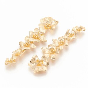 May include: Two gold-tone metal flower-shaped charms with a textured finish. Each charm is made up of five connected flower shapes.