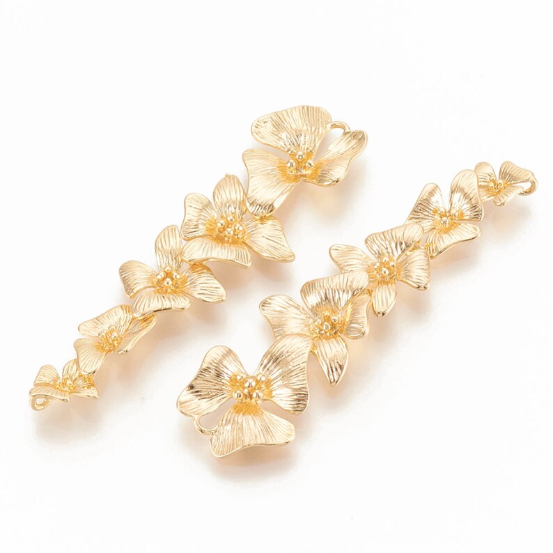 May include: Two gold-tone metal flower-shaped charms with a textured finish. Each charm is made up of five connected flower shapes.