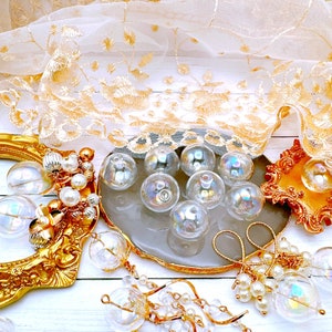 May include: A collection of iridescent glass beads on a white surface with a gold frame, a white lace fabric, and a gray and gold decorative plate. The beads are arranged in a circular pattern and are surrounded by other decorative elements.