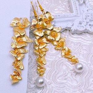 May include: A pair of gold-tone dangle earrings with a floral design and pearl accents.