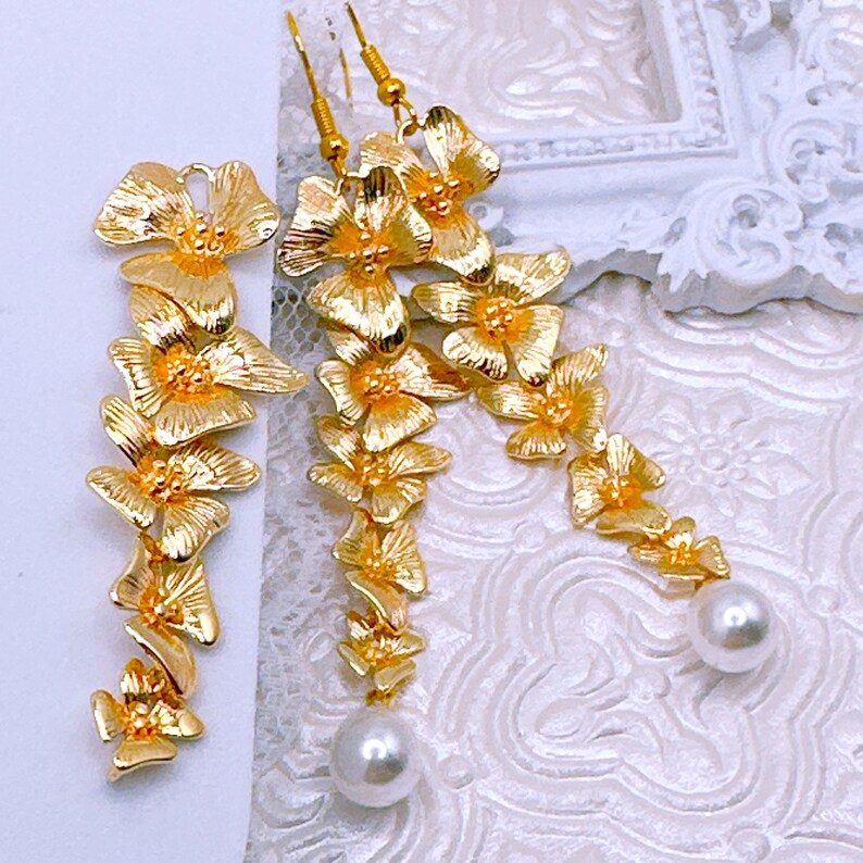 May include: A pair of gold-tone dangle earrings with a floral design and pearl accents.