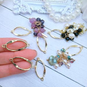 May include: Gold oval-shaped metal frames with a wavy edge. The frames are used for jewelry making and are shown with various beads and charms.