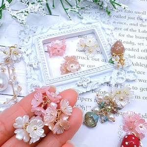 May include: Assortment of delicate pink and white flower charms with gold accents. The charms are made of resin and feature a cluster of flowers with a pearl center. The charms are perfect for adding a touch of elegance to jewelry, crafts, and other projects.