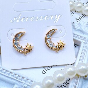 May include: Gold-toned crescent moon and star earrings. The moon-shaped earrings are encrusted with clear crystals and paired with a star. The earrings are displayed on a white card with the word "Accessory" printed on it.