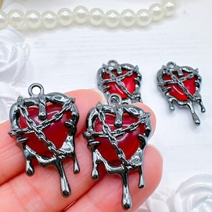 May include: Heart-shaped charms with a dark gunmetal finish, featuring a red center and a chain design. The charms have a dripping effect at the bottom. These gothic-style charms are ideal for jewelry making.